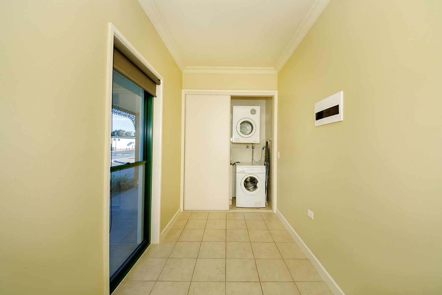 A narrow hallway with a sliding glass door on the left, a washing machine and dryer in the center, and a small window on the right.