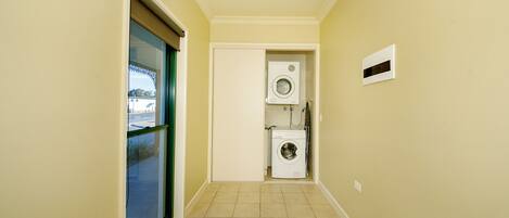 A narrow hallway with a sliding glass door on the left, a washing machine and dryer in the center, and a small window on the right.