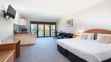 A hotel room with a bed, a desk, a television, a dining table with chairs, and a balcony with a view.