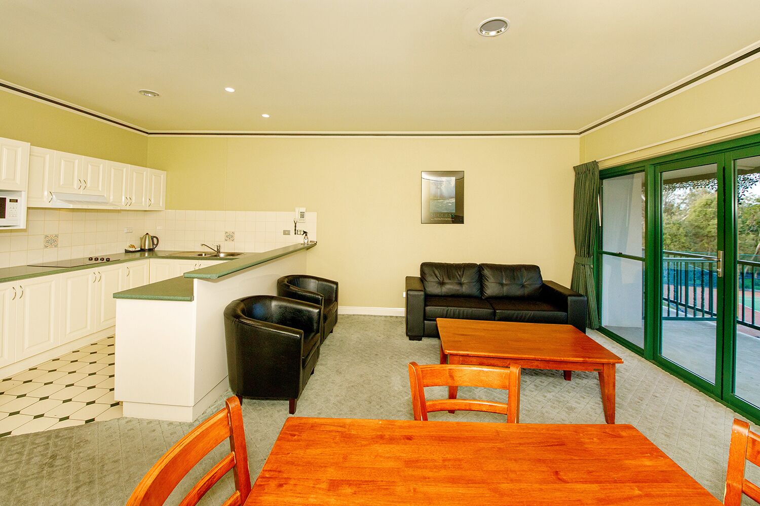 A compact living space with a kitchenette, a sofa, a dining table, and a view through a glass door.