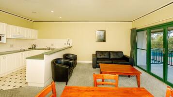 A compact living space with a kitchenette, a sofa, a dining table, and a view through a glass door.