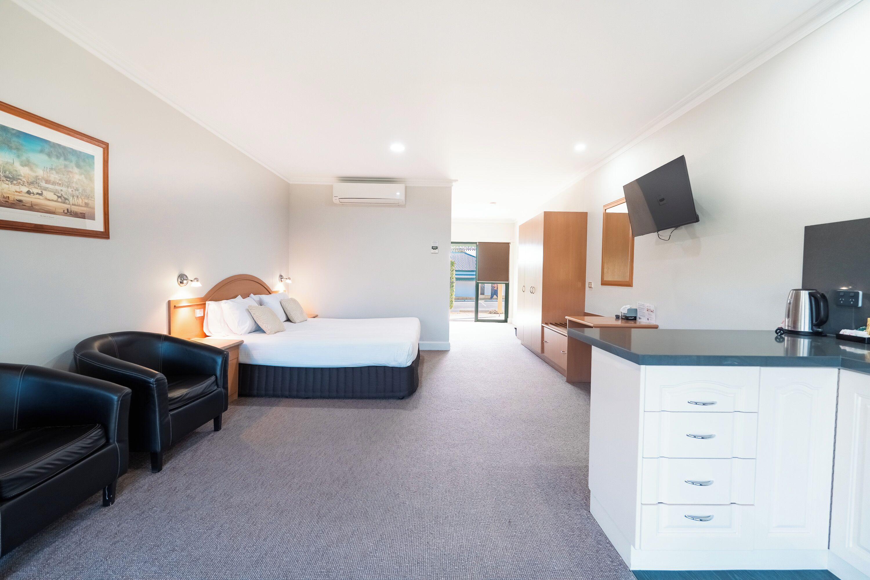 A hotel room with a bed, a desk, a chair, a television, and a painting on the wall.
