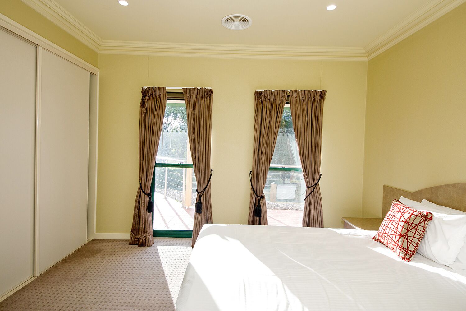 Habitación de hotel con una cama grande, dos ventanas con cortinas, vistas al exterior y una lámpara en el techo.