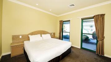 A hotel room with a bed, a nightstand, a window with curtains, and a view of the outside.