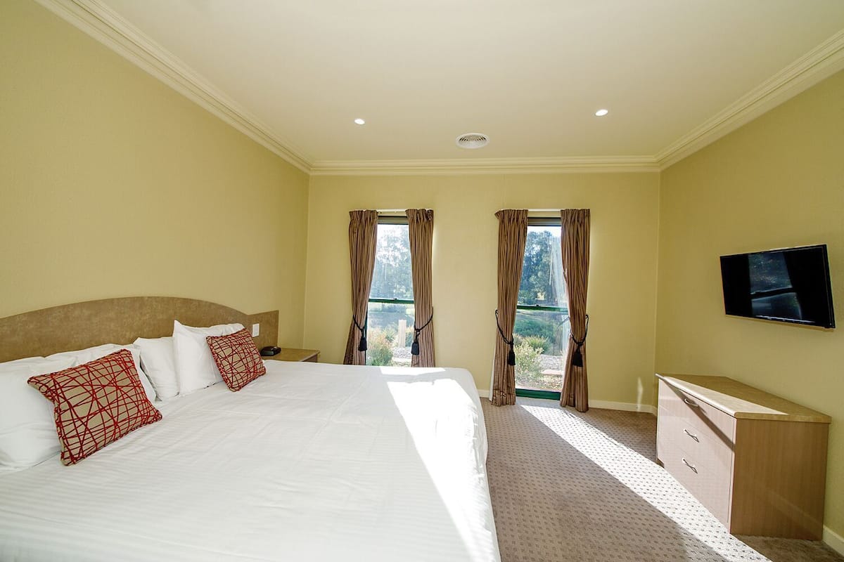 A hotel room with a large bed, a TV, a dresser, and a view through the curtains.