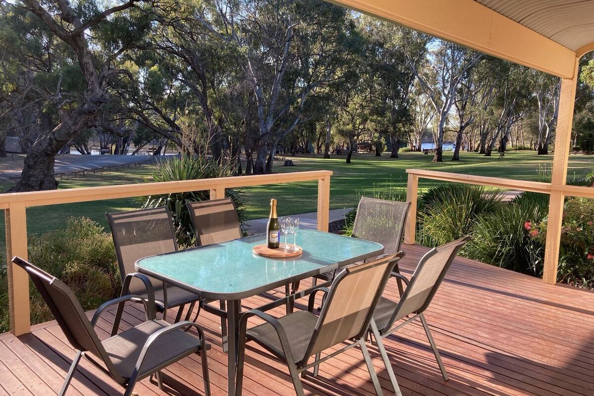 An outdoor patio with a table and chairs, a bottle of champagne, and a view of a golf course.