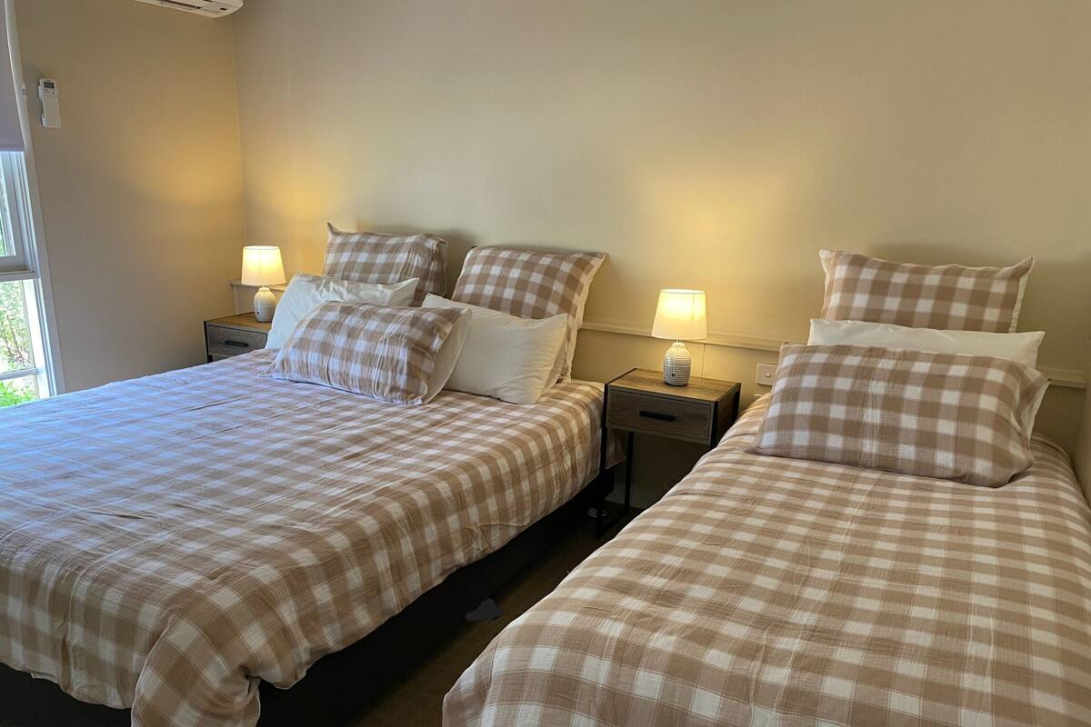 A hotel room with two beds, each with a checkered bedspread and matching pillows. There are bedside tables with lamps and a small drawer.