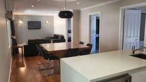 Una cocina moderna con encimera blanca, un fregadero y una zona de comedor con mesa y sillas.
