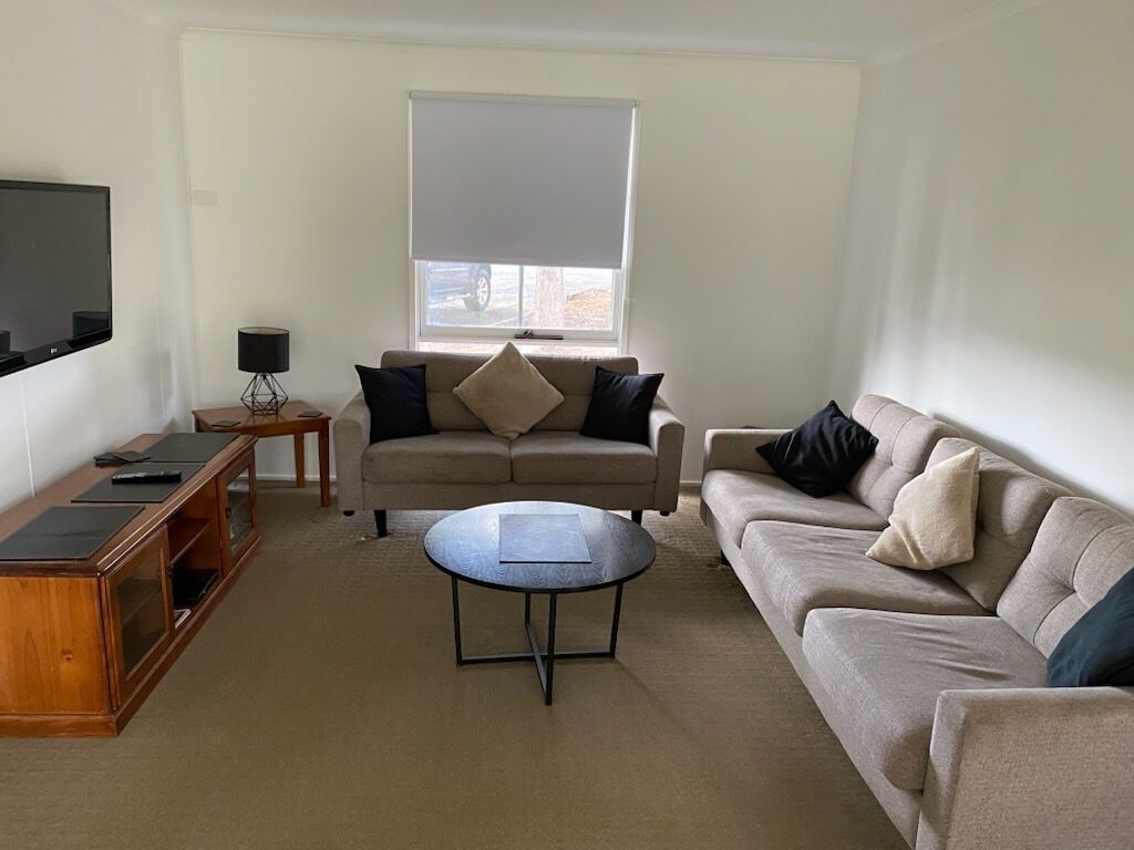 A living room with a sofa, a coffee table, a TV, and a window with blinds.