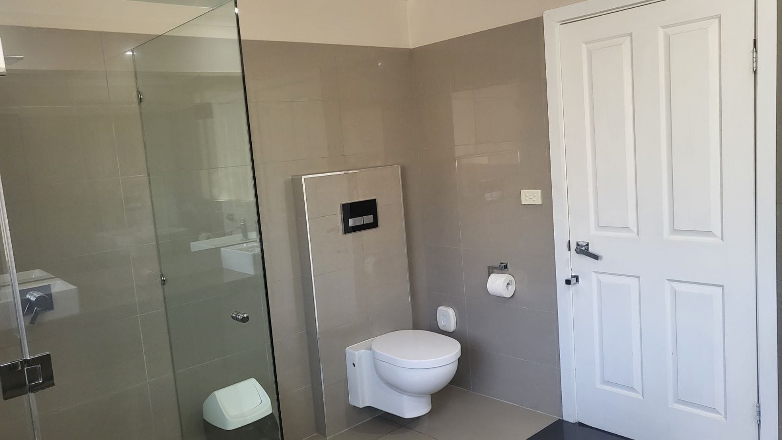 A bathroom with a glass shower enclosure, a toilet, and a white door.