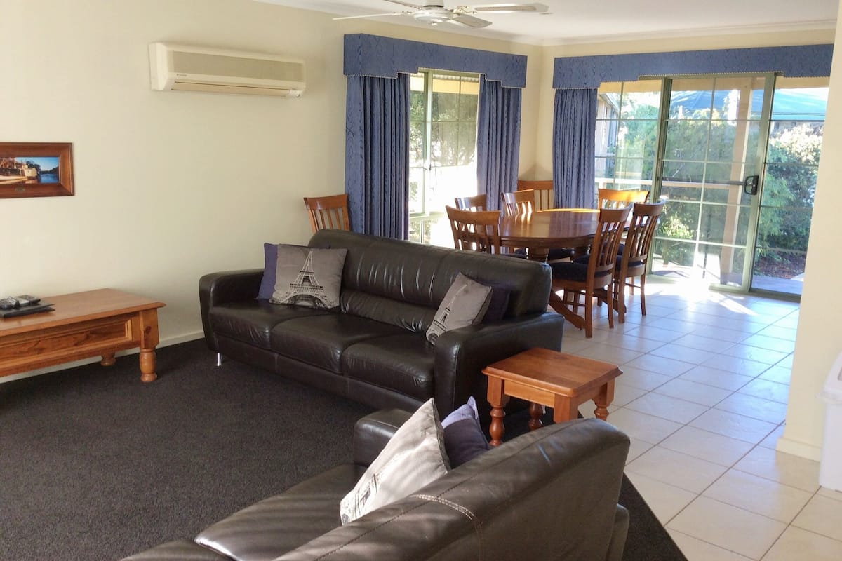 A living room with a black leather sofa, wooden coffee table, and a dining area with a wooden table and chairs.