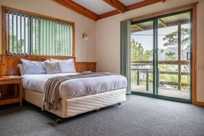 A bedroom with a bed, a nightstand, a window with blinds, and a view of the outdoors. - Freycinet Cottage 2 (Coles Bay)