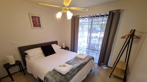 A hotel room with a bed, a ceiling fan, a window with curtains, a bedside table, and a coat rack. - Barossa Country Cottages (Lyndoch)