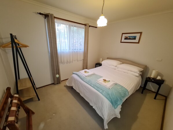 A neatly arranged bedroom with a bed, bedside tables, a hanging light fixture, a window with curtains, and a framed picture on the wall. - Barossa Country Cottages (Lyndoch)