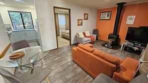 A modern living room with a glass dining table, a sofa, a TV, and a fireplace. - Barossa Country Cottages (Lyndoch)