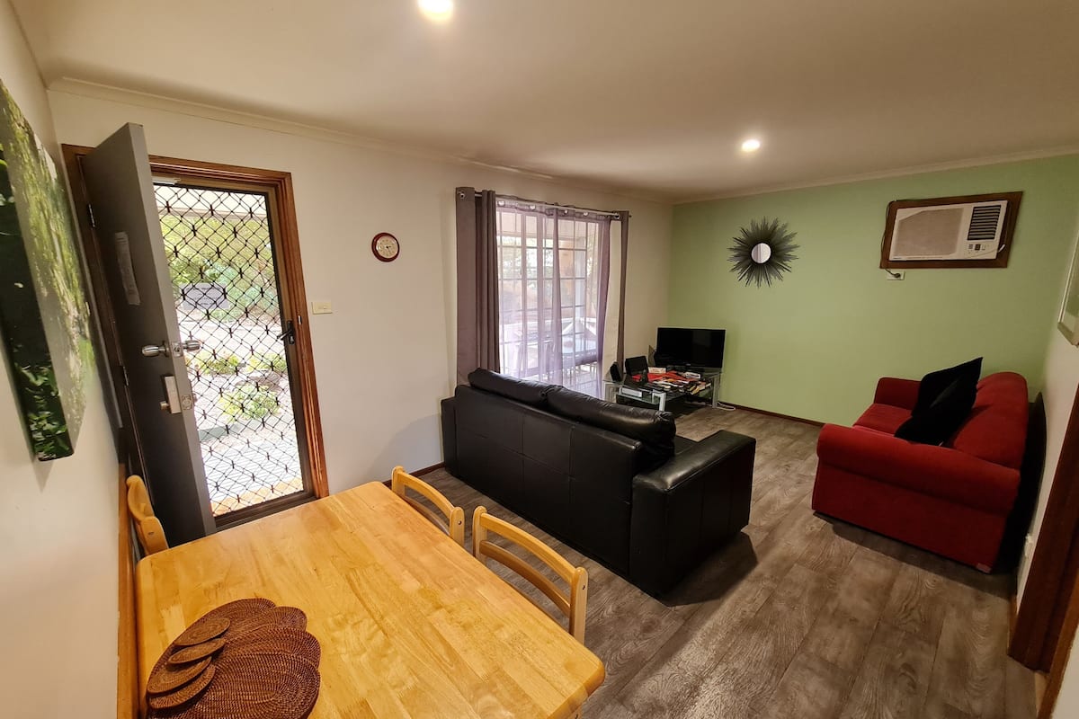 A living room with a sofa, a red couch, a wooden dining table with chairs, a TV, and a window with curtains.