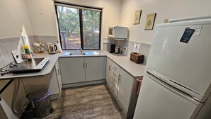A compact kitchen with a built-in stove, a sink, a refrigerator, and a window providing a view of trees. - Barossa Country Cottages (Lyndoch)