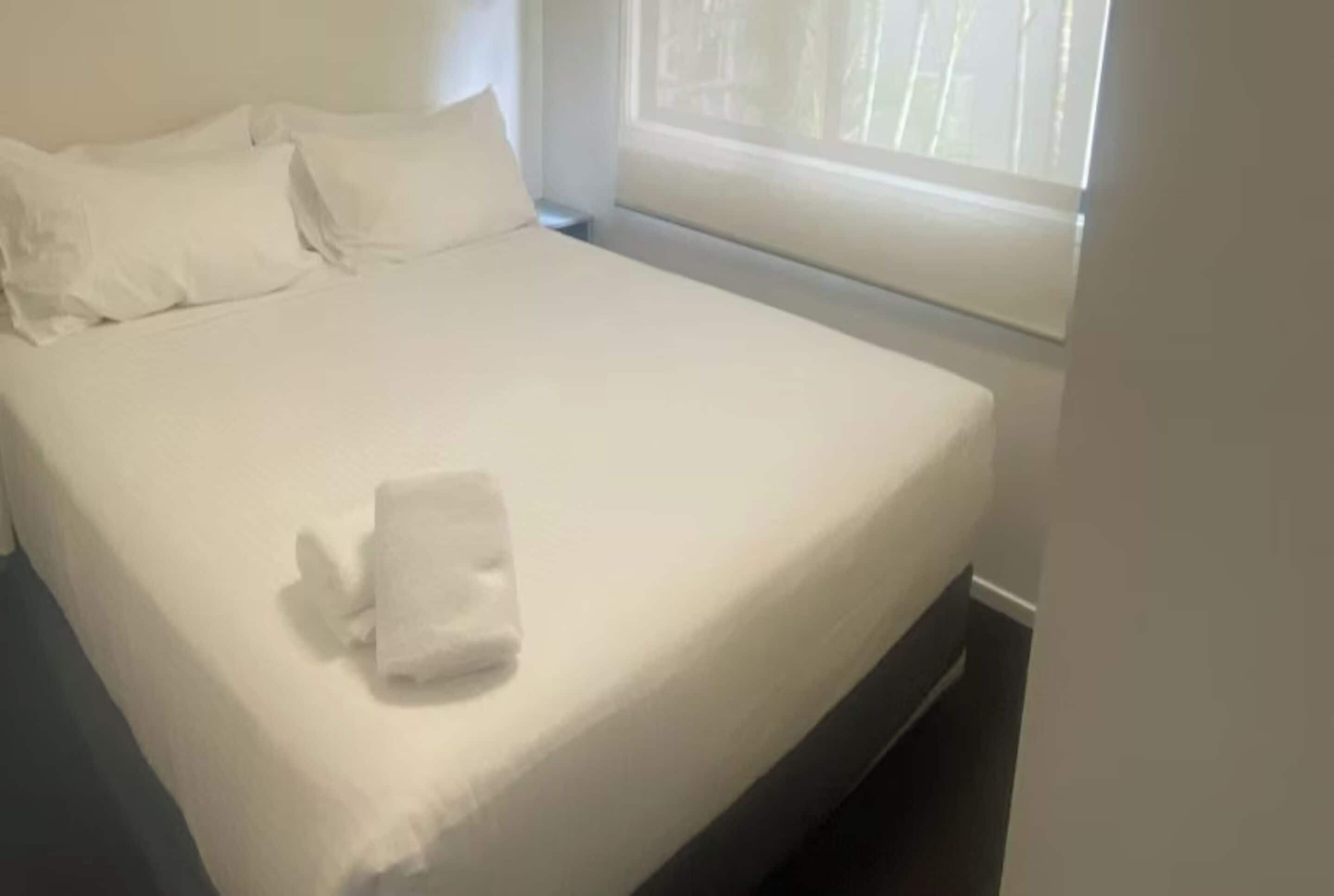 A neatly made bed with white linens and a folded towel on the bed.