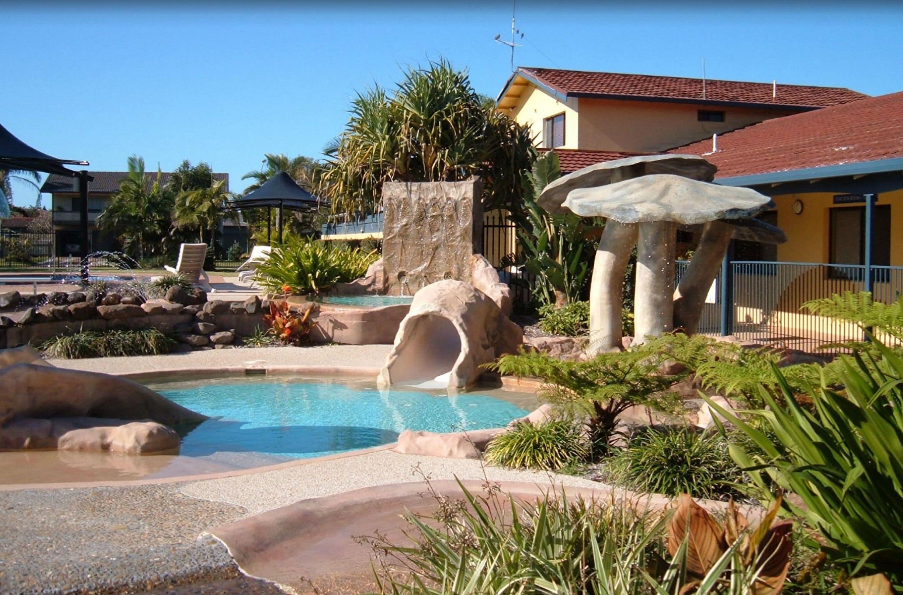 A pool area with a water slide, palm trees, and a building with a red roof.