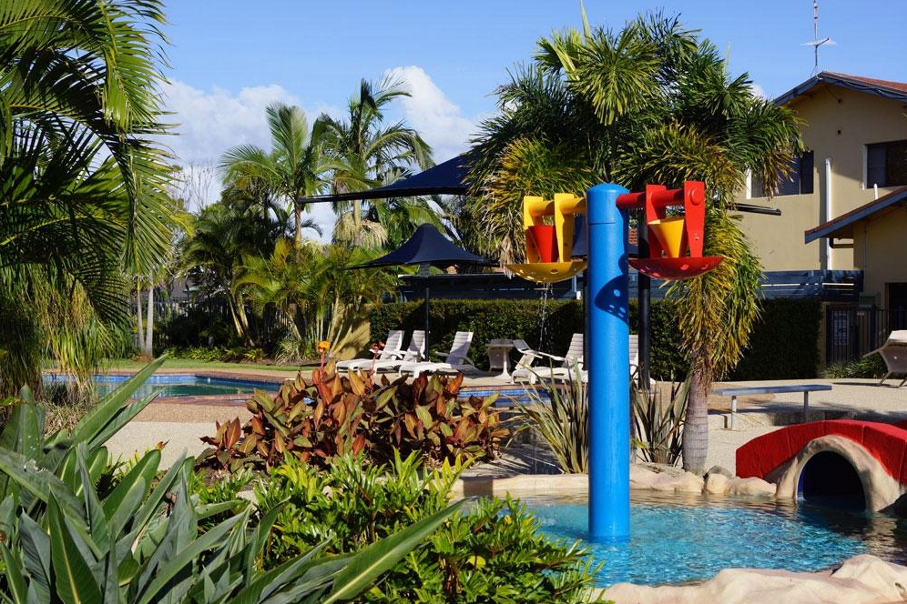 A pool area with a water slide, lounge chairs, and palm trees.