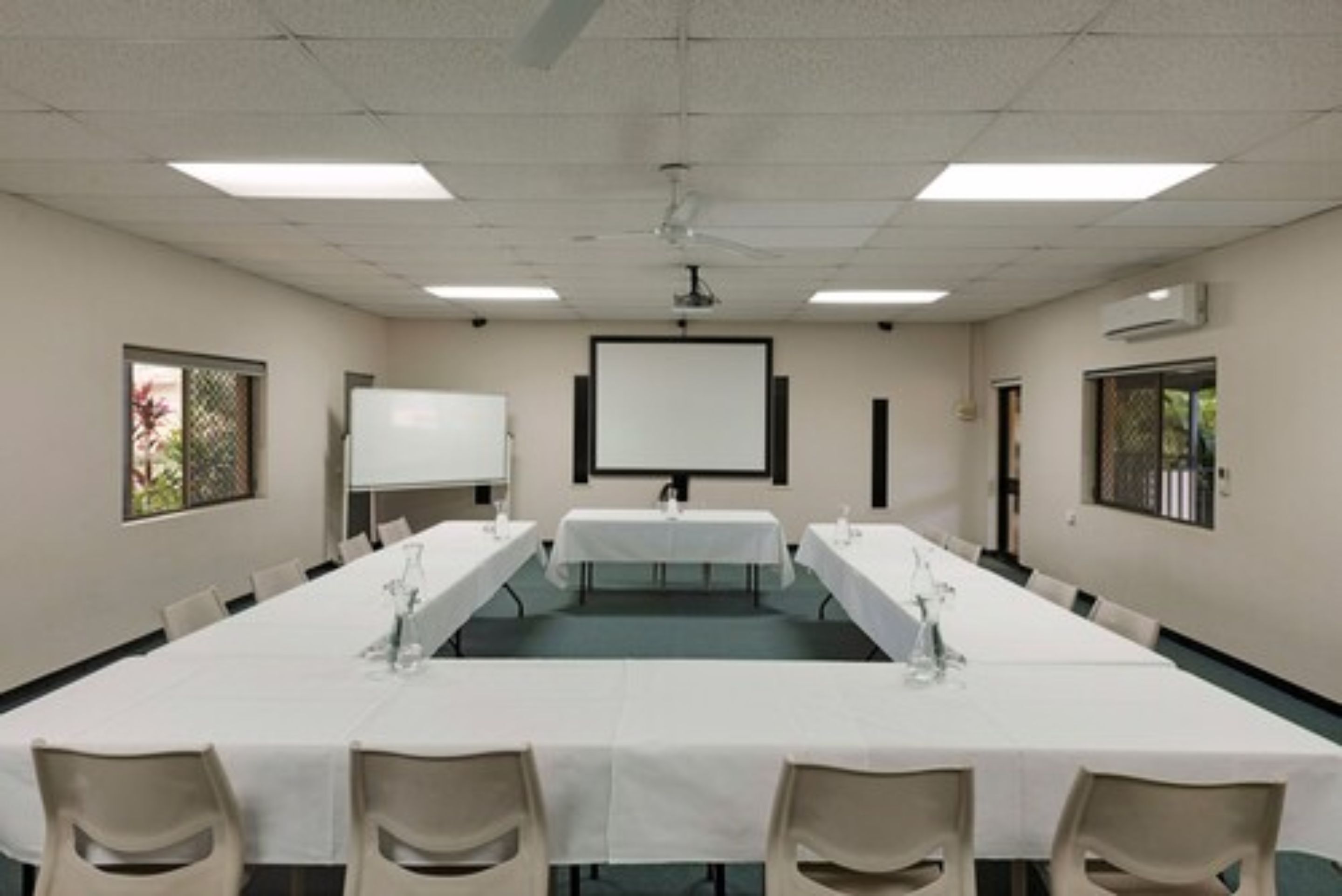 Une salle de conférence équipée d’une longue table, de chaises, d’un écran de projection et d’un tableau blanc.