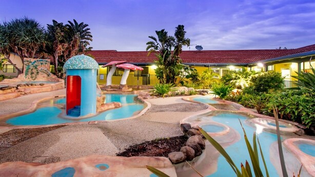 A pool area with multiple water features and a building in the background. - Discovery Parks - Ballina (East Ballina)