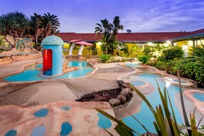 Uma área de piscina com diversas fontes e um edifício ao fundo.