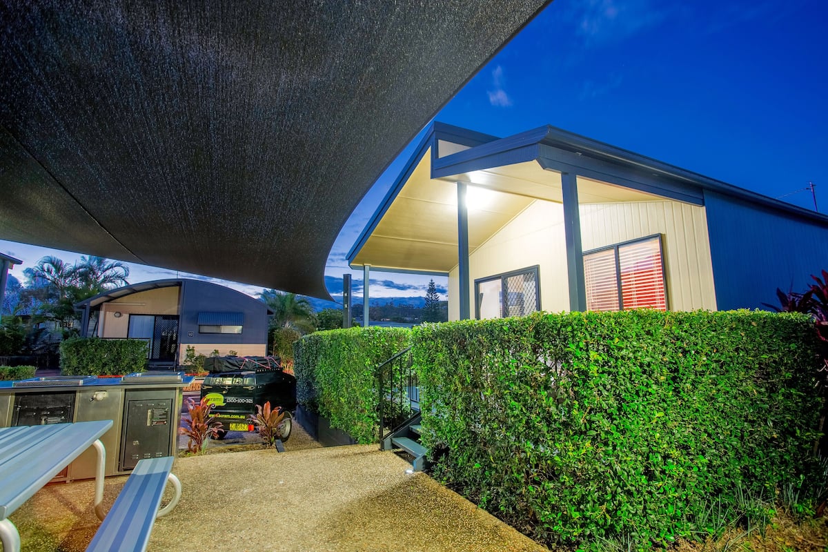A covered outdoor area with a barbecue, a table, and a staircase leading to a building.