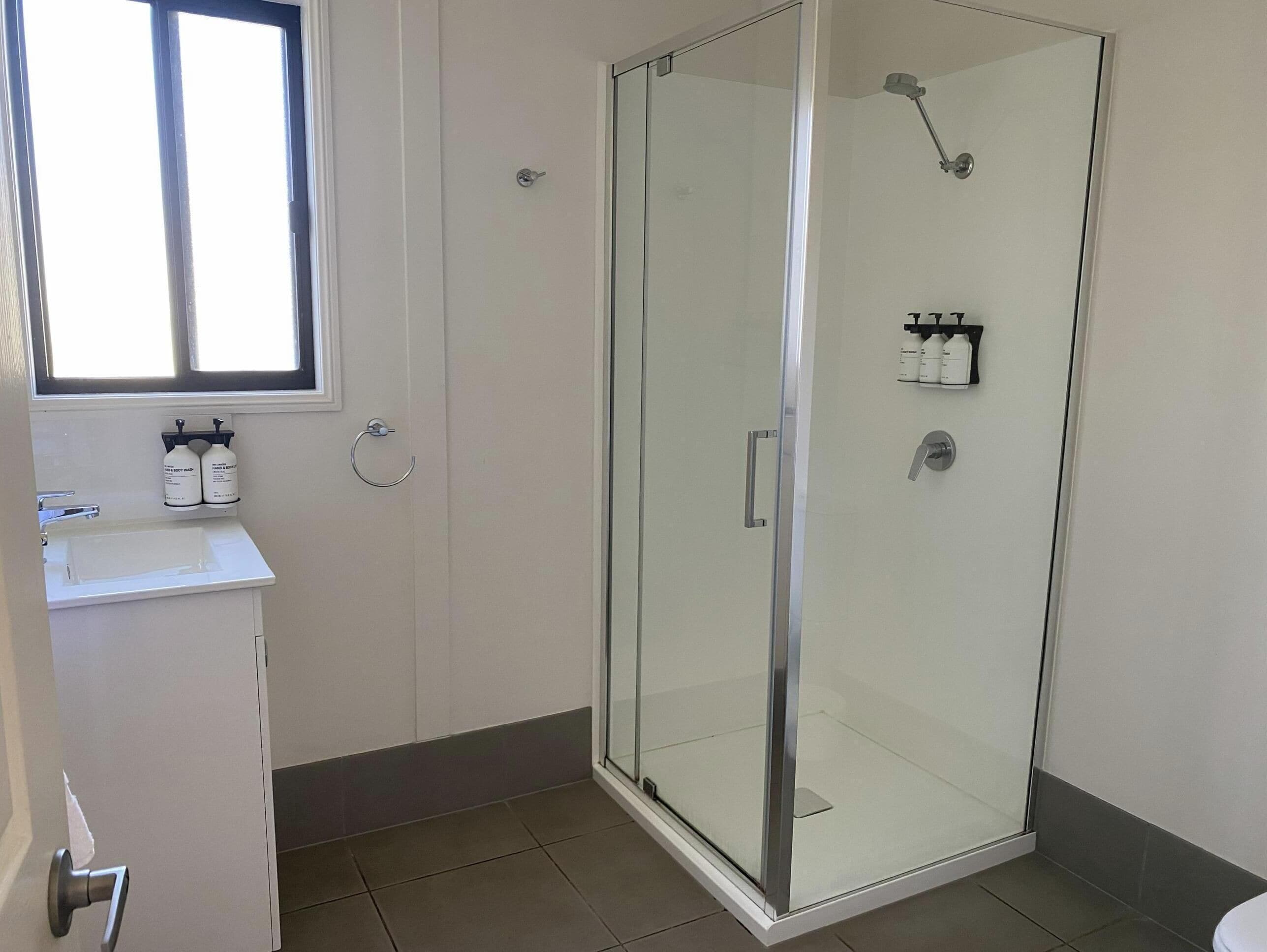 Un baño con ducha de vidrio, lavamanos y ventana.
