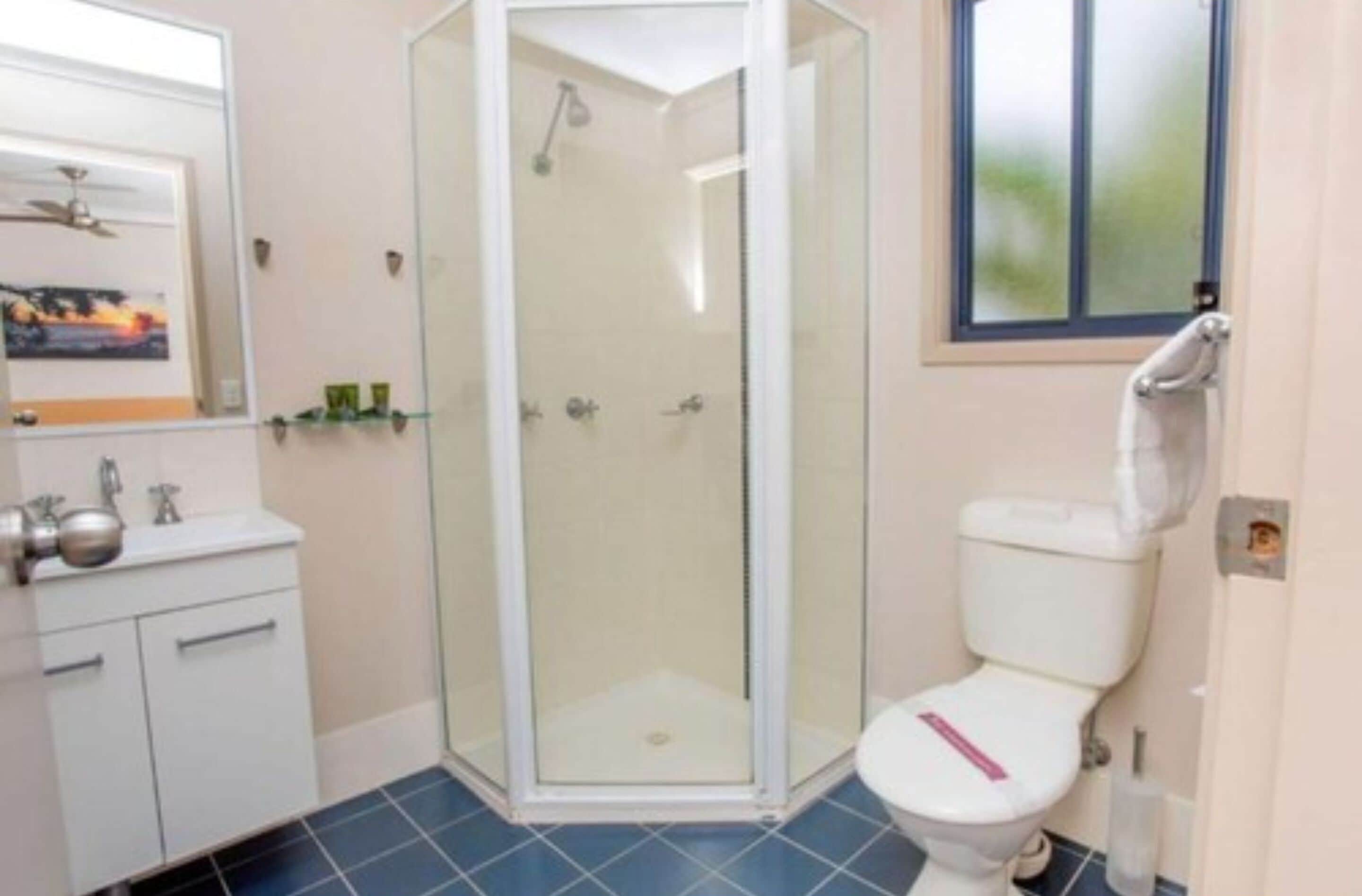 Un baño con ducha de vidrio, inodoro blanco y lavamanos con espejo.