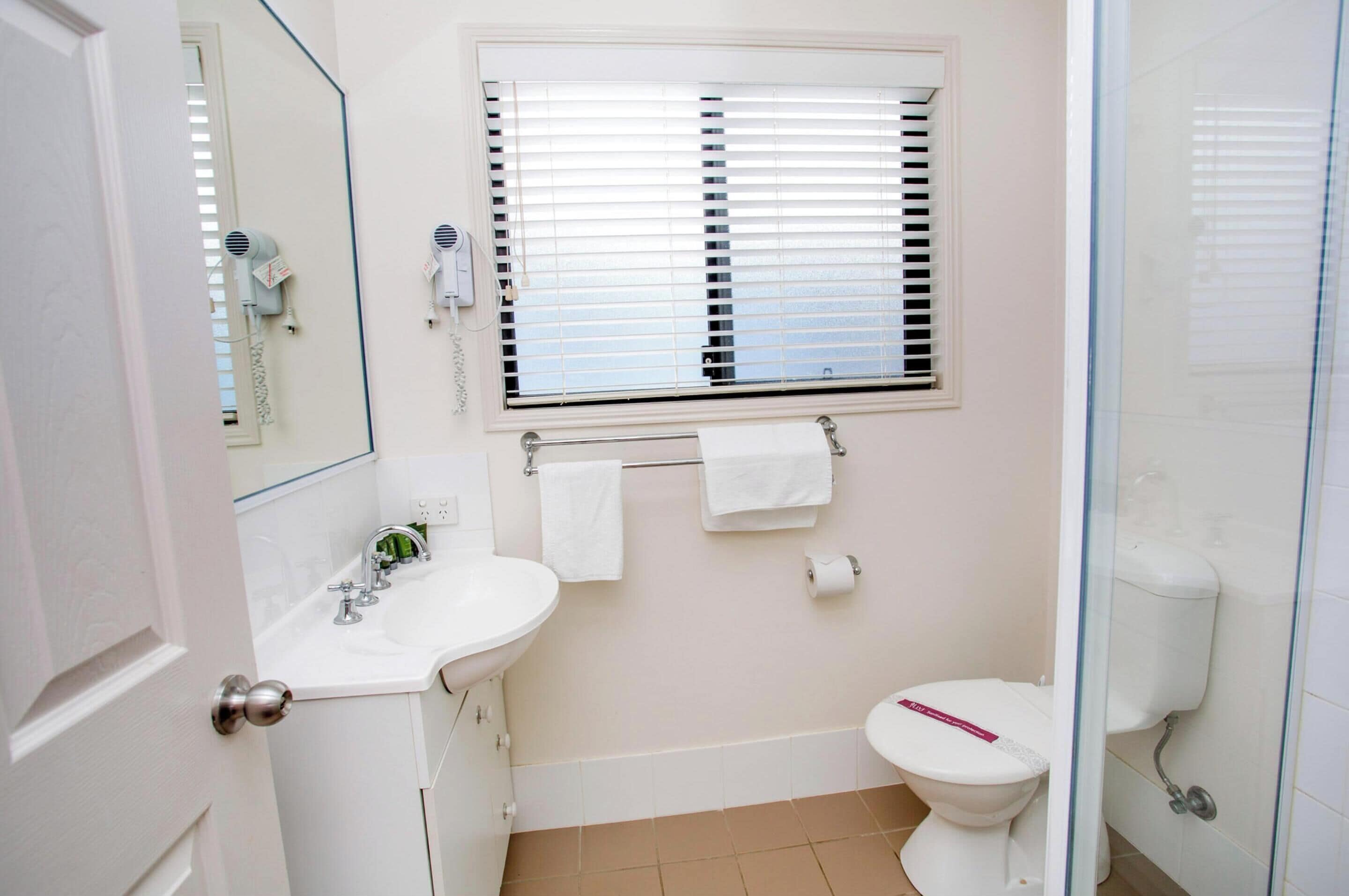 A bathroom with a sink, toilet, and window blinds.