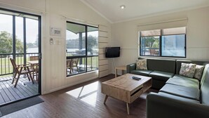 A living room with a sofa, a coffee table, a TV, and a balcony with outdoor furniture. - Discovery Parks - Ballina (East Ballina)
