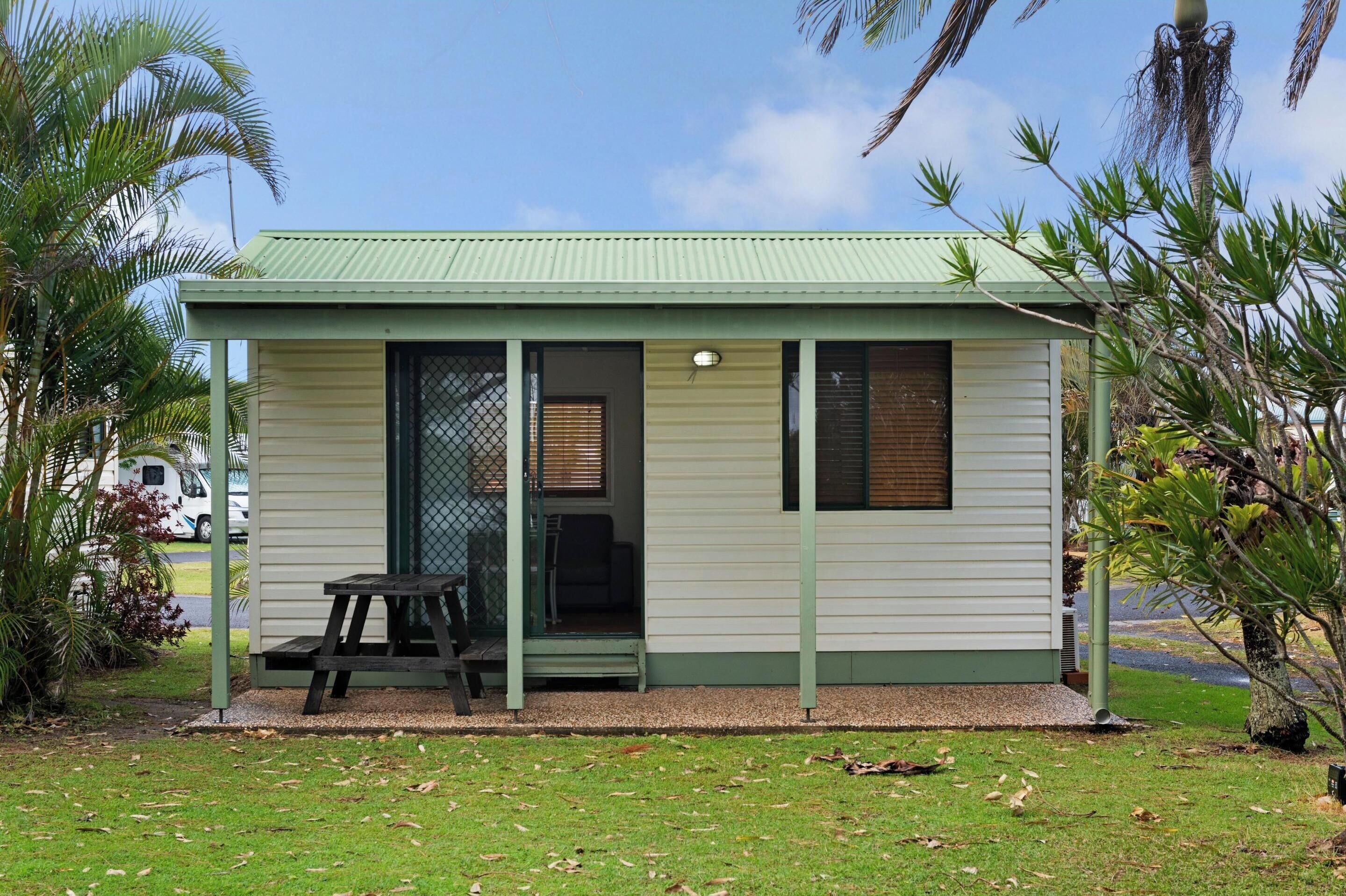 A small, single-story building with a green roof and a covered patio area.
