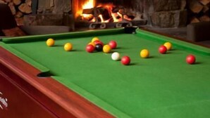 A pool table with balls in front of a stone fireplace with a fire. - Hotel High Plains (Dinner Plain)