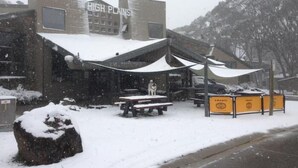 A building named 'HIGH PLAINS' with outdoor seating and snow on the ground. - Hotel High Plains (Dinner Plain)