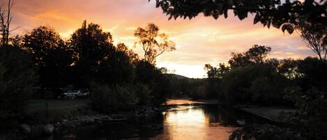 Un río al atardecer, con árboles a ambos lados y un puente a lo lejos.