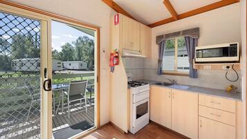 A compact kitchen with a gas stove, oven, and microwave, wooden cabinets, and a sliding glass door leading to an outdoor deck.