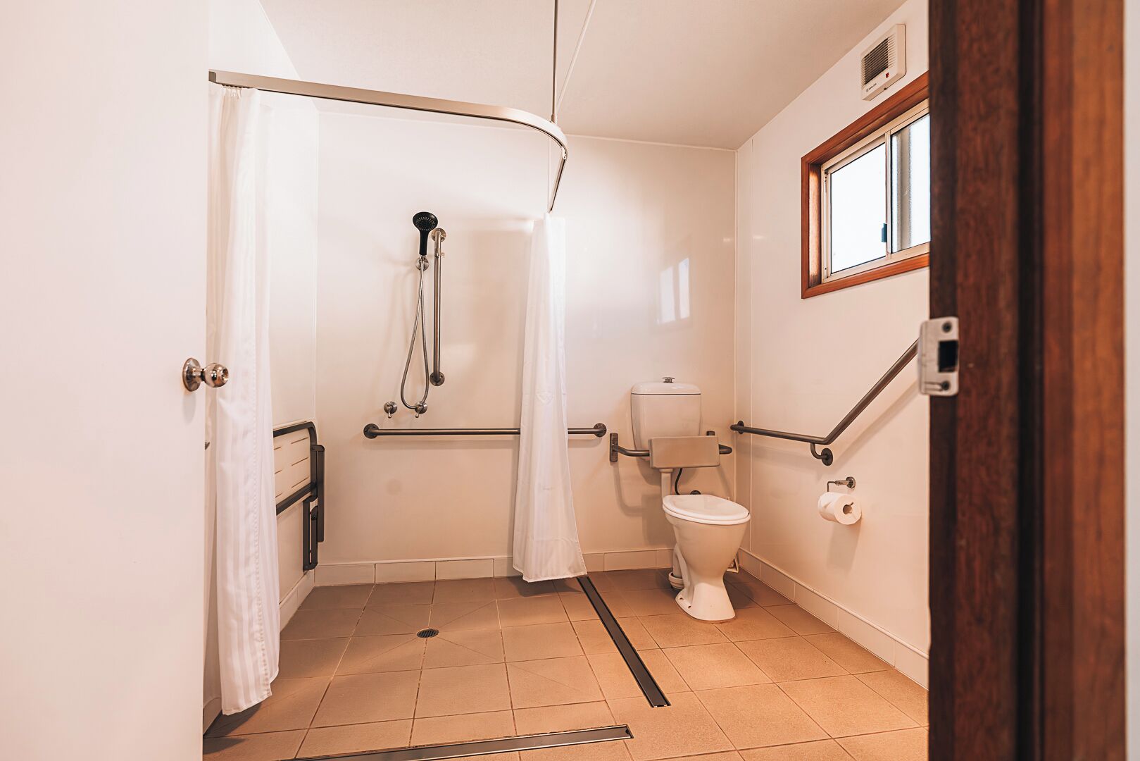 A small, single-room bathroom with a shower, toilet, and a window.