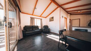 A spacious living area with a dark wood floor, a black leather sofa, a black leather chair, and a dining table with chairs.