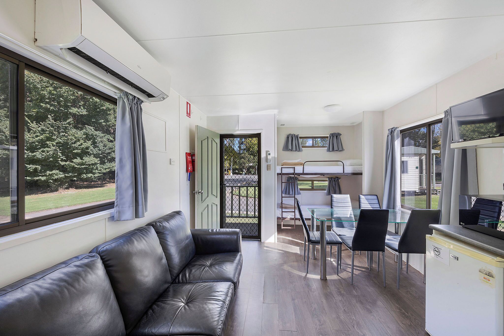 Een moderne kamer met een leren bank, een eettafel met stoelen, een kitchenette en een groot raam met gordijnen.