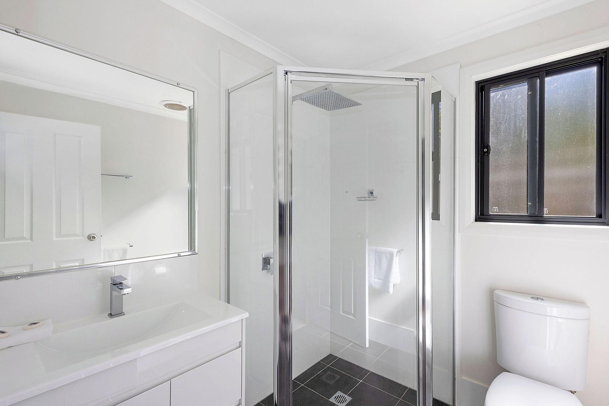 Een moderne badkamer met een douchecabine van glas, een witte wastafel en een toilet.