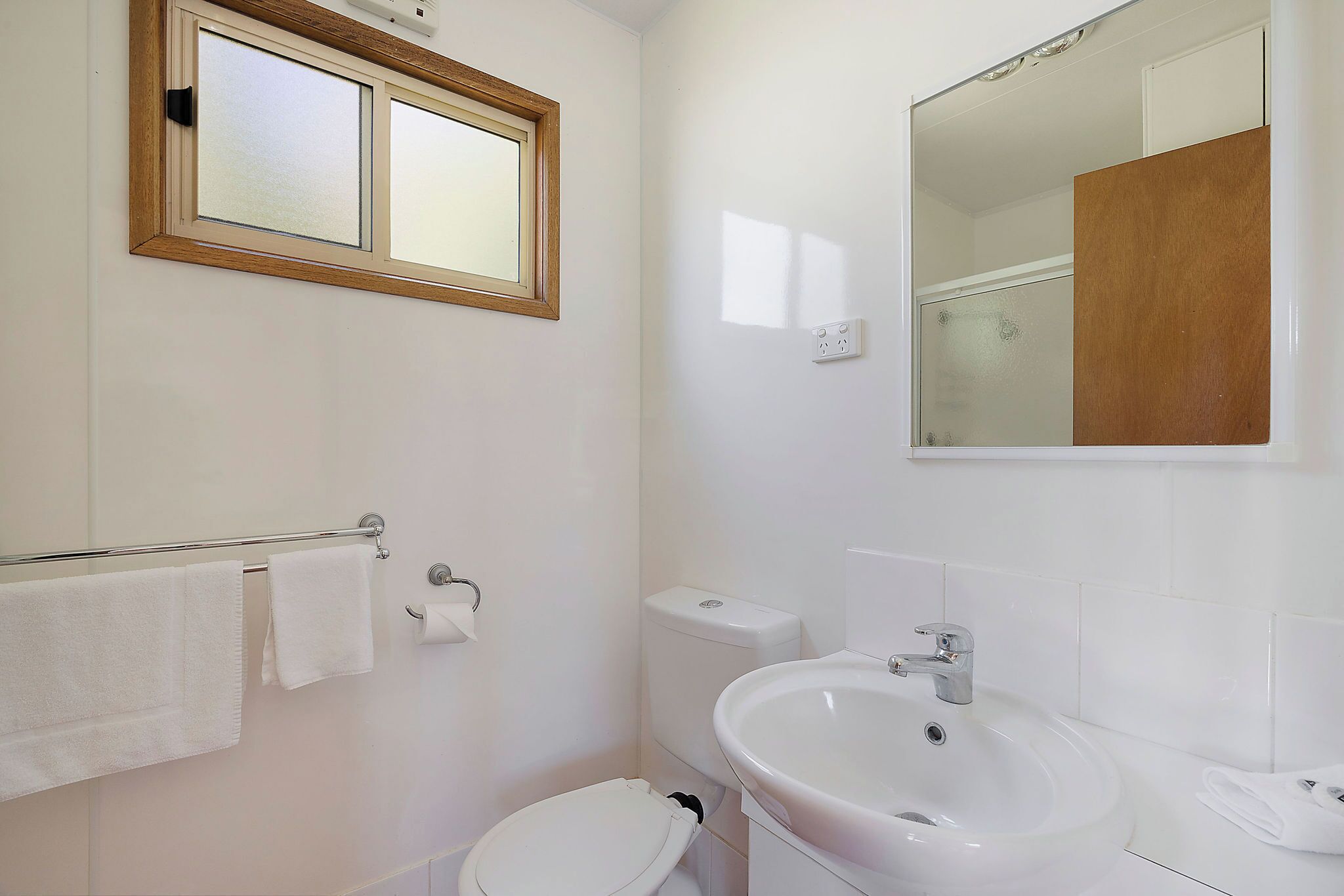 Un baño con inodoro, lavamanos y perchero para toallas.
