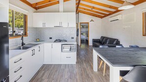 A modern kitchen with white cabinets, a built-in oven, and a large island. There is a dining area with a table and chairs. - Reflections Tumut River (Tumut)