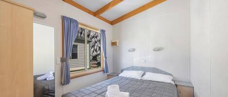 Un dormitorio con cama, mesita de noche, espejo y ventana con cortinas.
