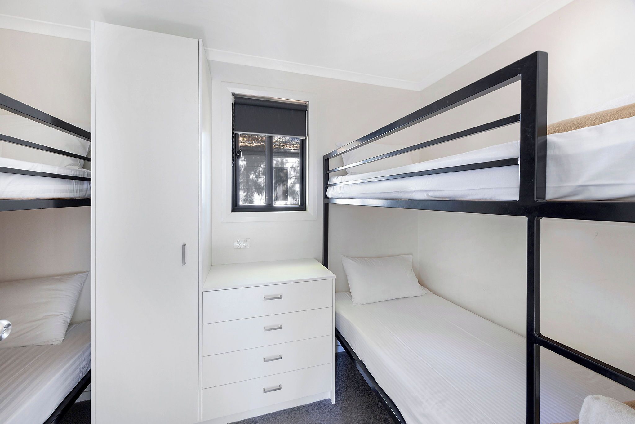 A bunk bed room with a white wardrobe and a window.