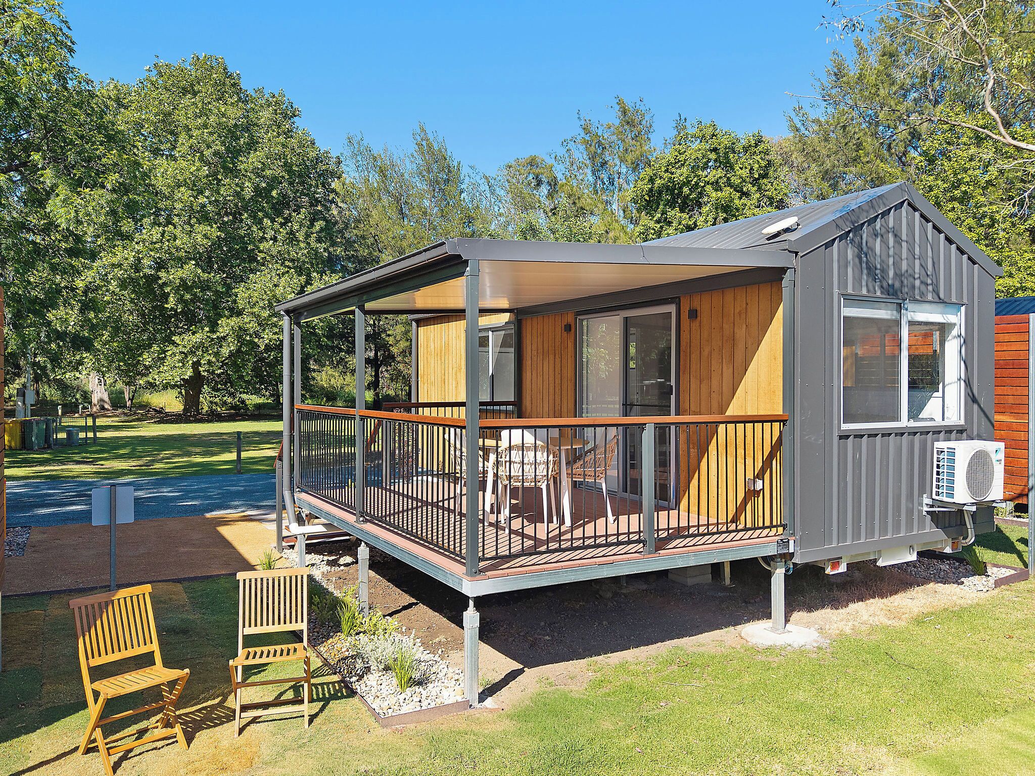 Een klein huisje met balkon, een houten terras en een tuin met stoelen.