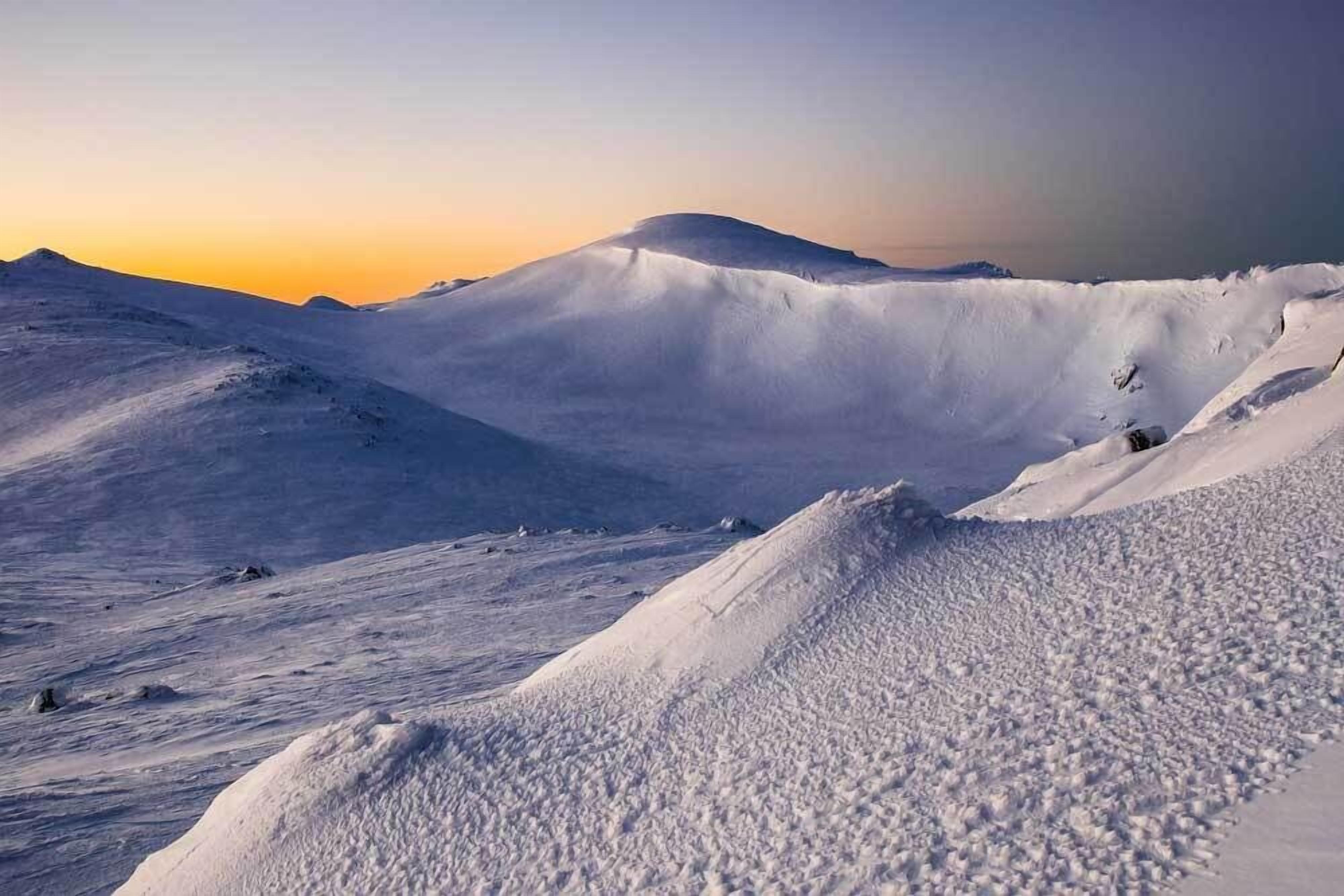 Paisaje nevado con terreno ondulado y montañas a la distancia.