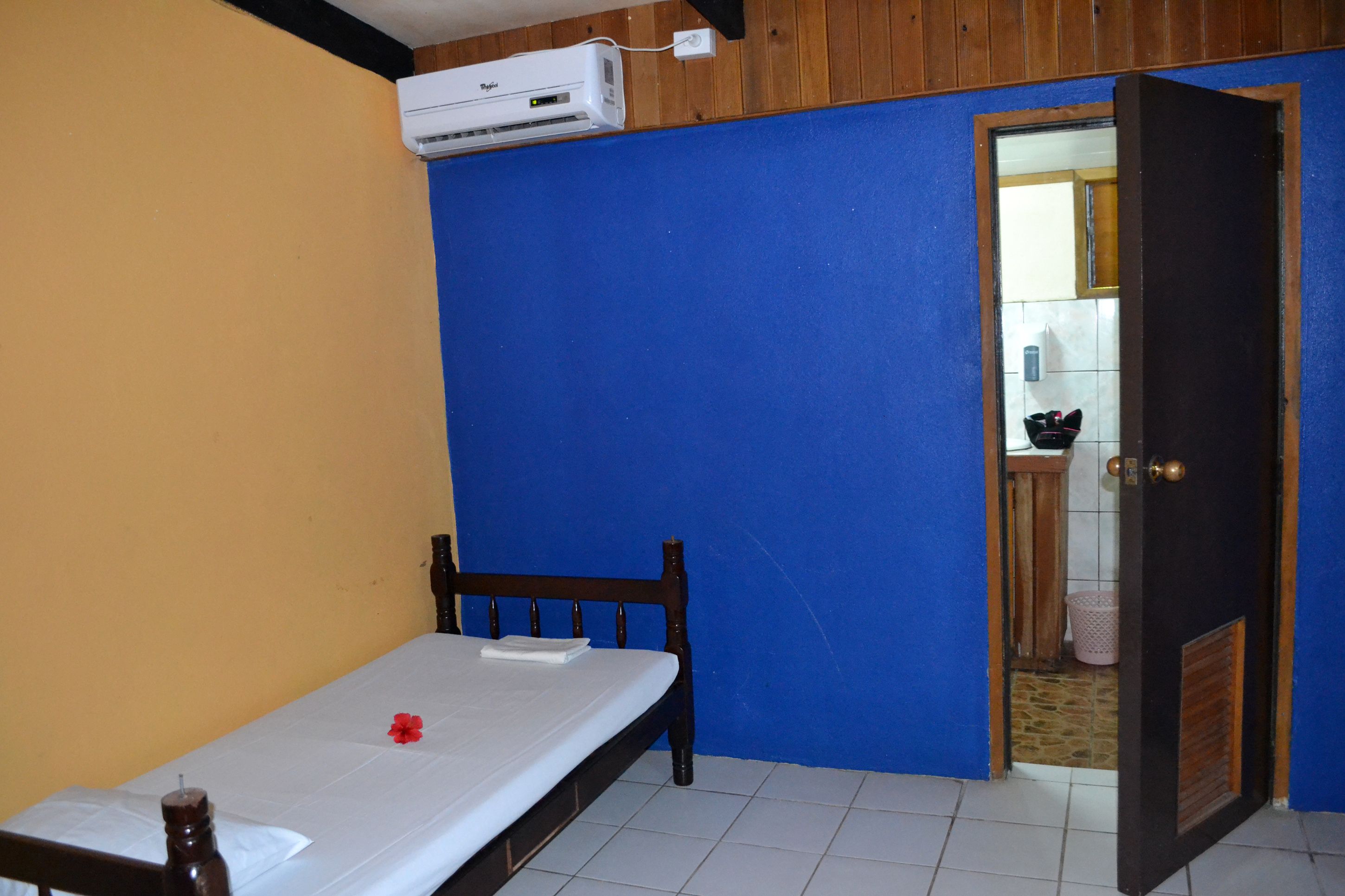 A room with a bed, an air conditioner, a wooden door, and a blue wall.