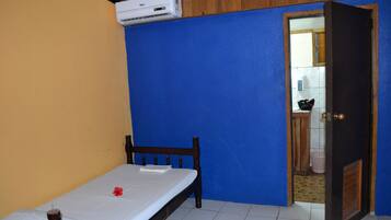 A room with a bed, an air conditioner, a wooden door, and a blue wall.