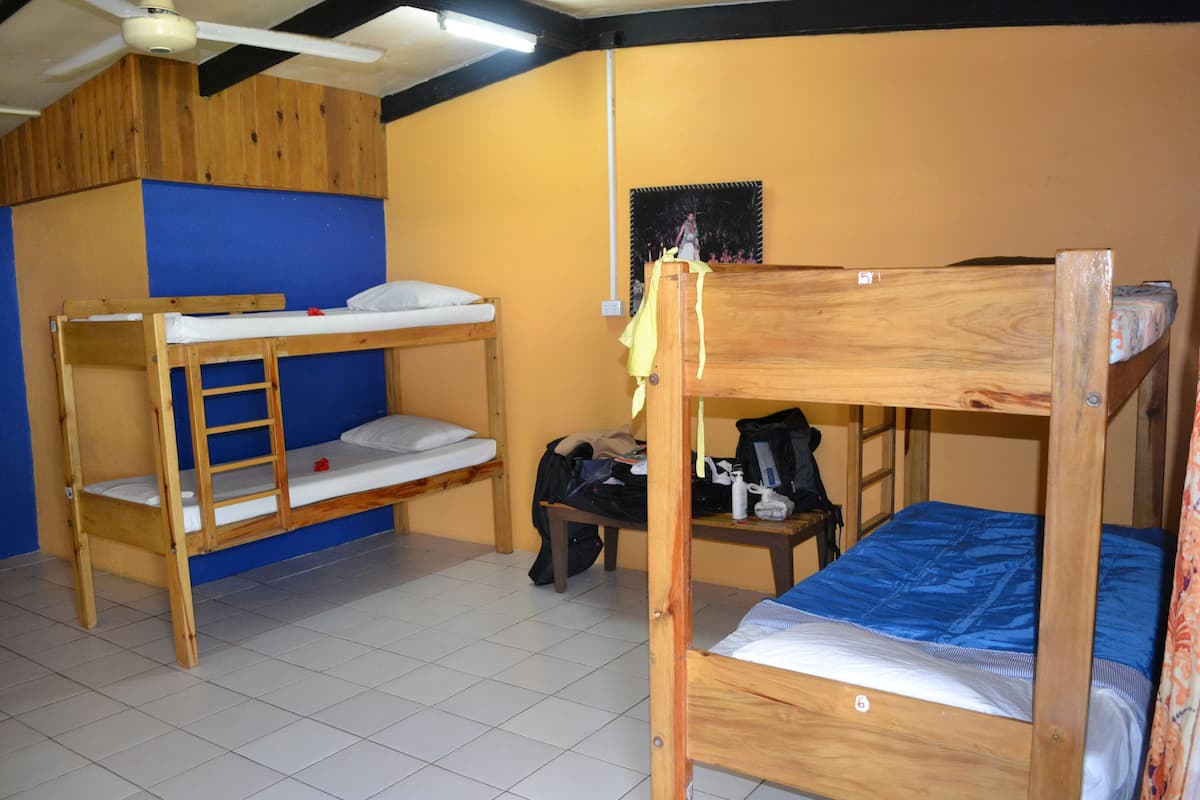 A dormitory room with bunk beds, a ceiling fan, and a small table with personal items.